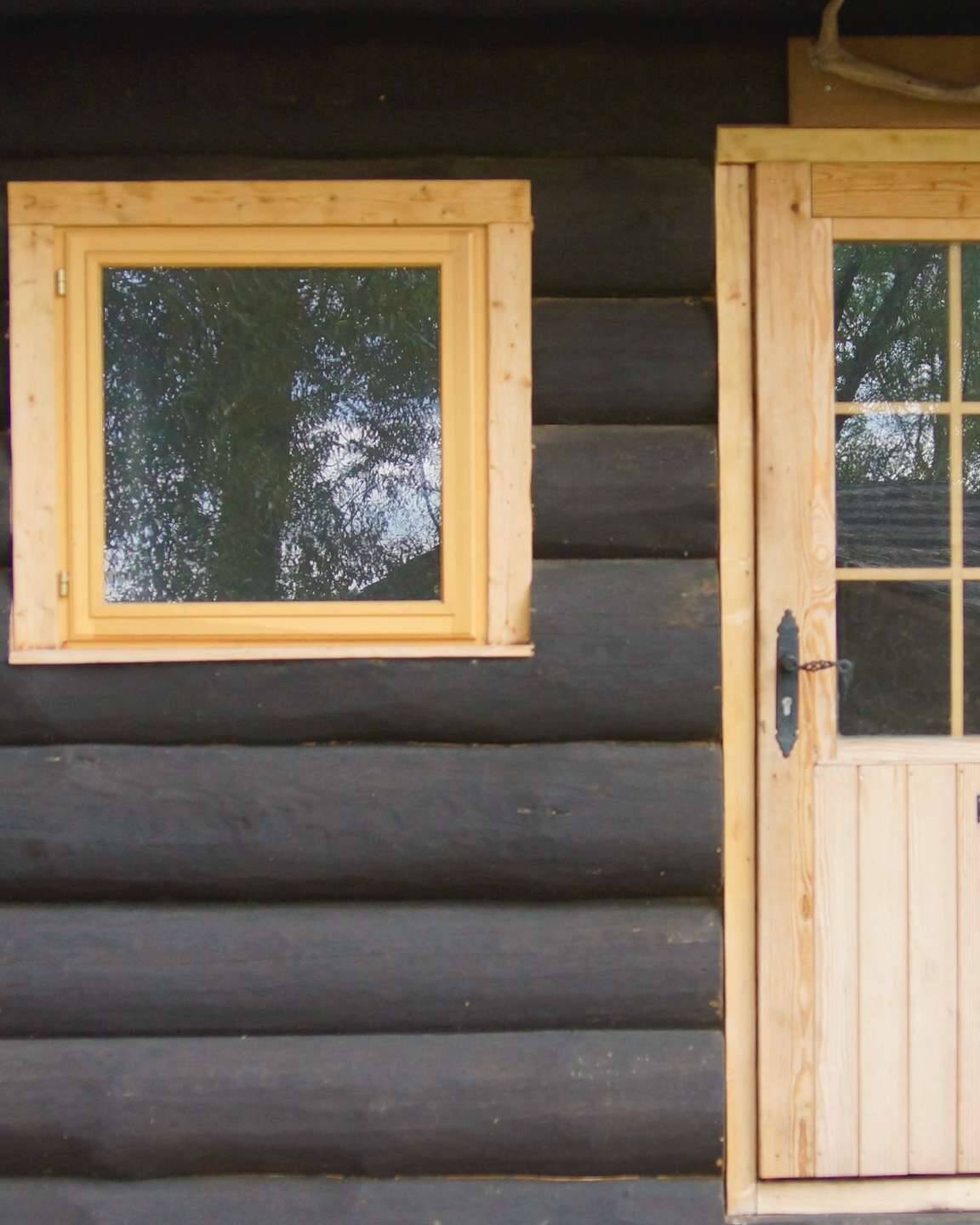 Schwarzes Rundstamm Ferienhaus mit naturbelassener Tür und Fenster