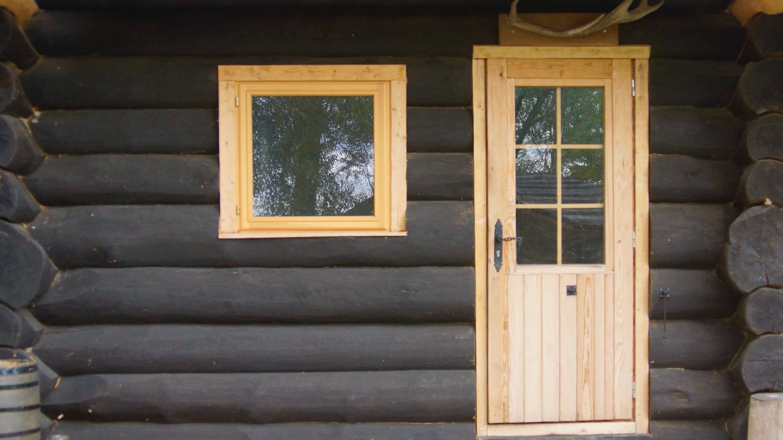 Schwarzes Rundstamm Ferienhaus mit naturbelassener Tür und Fenster